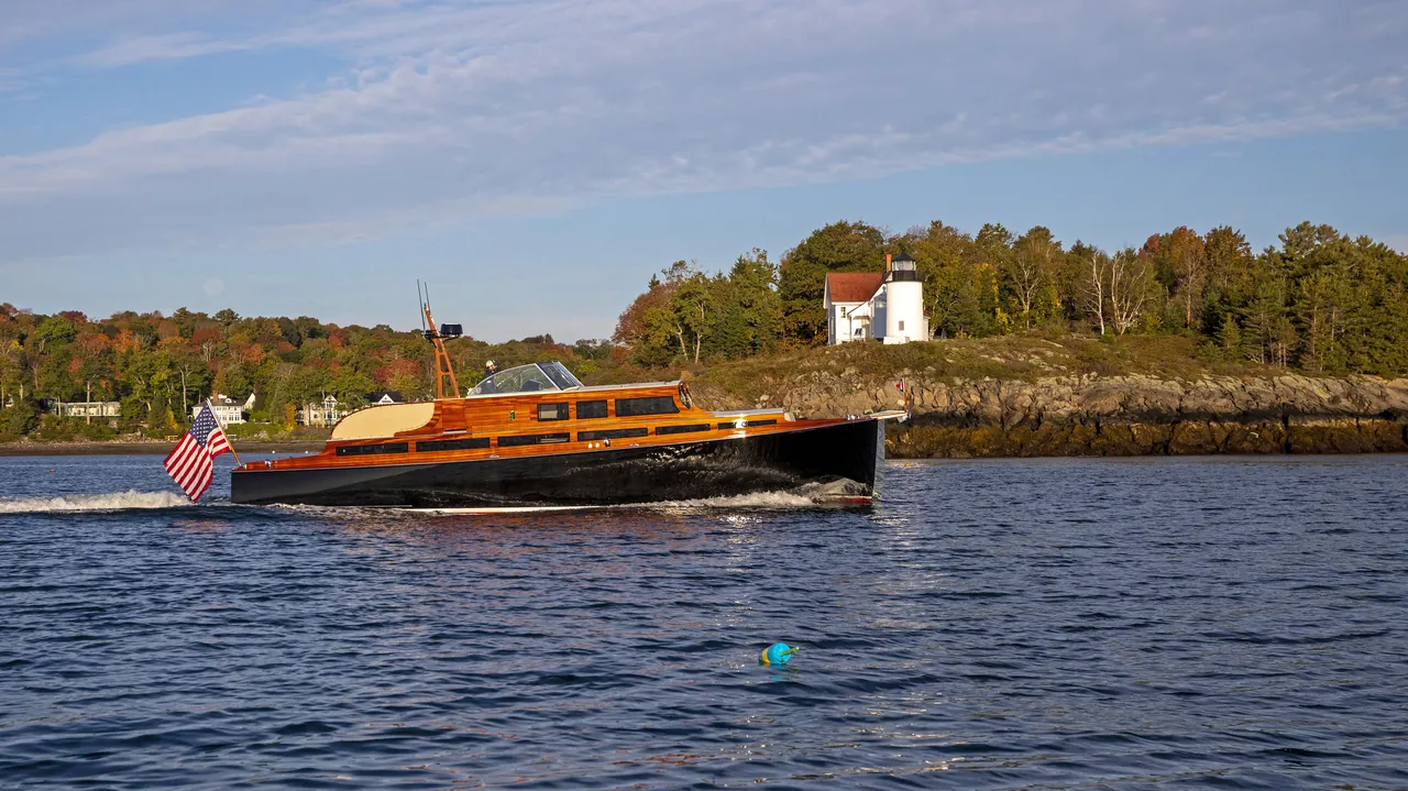 Classic varnished launch running past a lighthouse